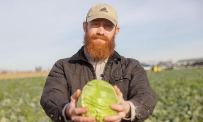 farmer wearing baseball hat holding cabbage in outstretched arms