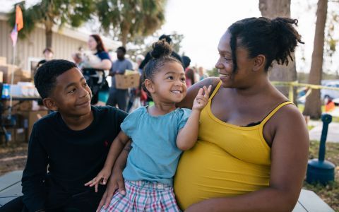 A pregnant mom smiling with her two children.