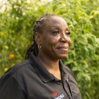 A woman smiling in front of a garden.
