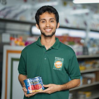 A volunteer holding two cans of food in a pantry.